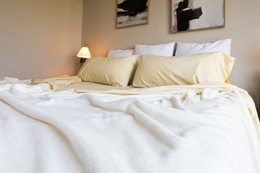 Neatly made bed with white and beige bedding in a bedroom setting.