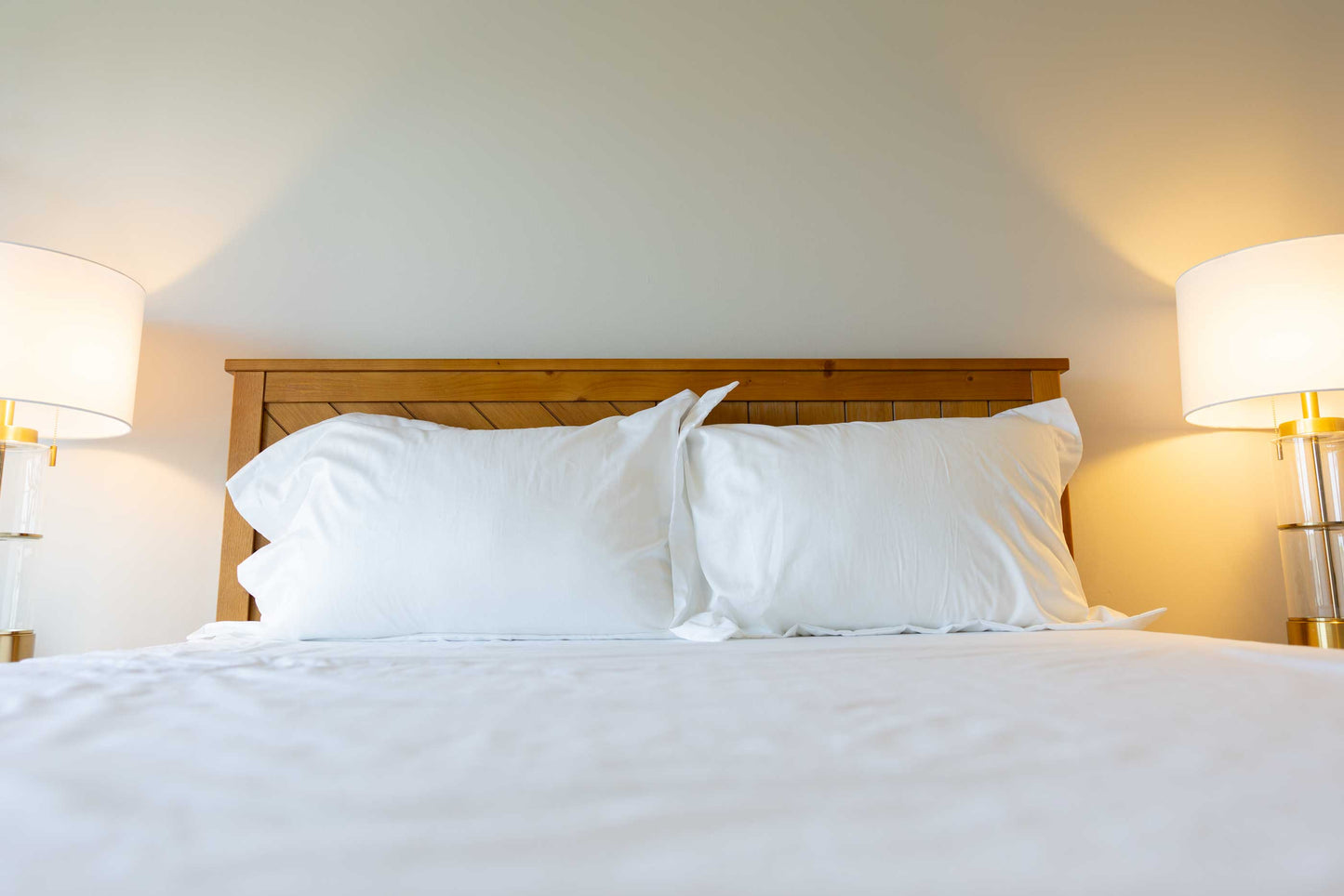 Bed with white pillows, split sheet set and wooden headboard in a softly lit bedroom.
