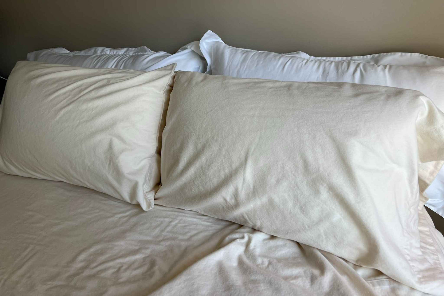 Two pillows with flannel pillowcases and two pillows with pillow shams on a bed with a neutral background