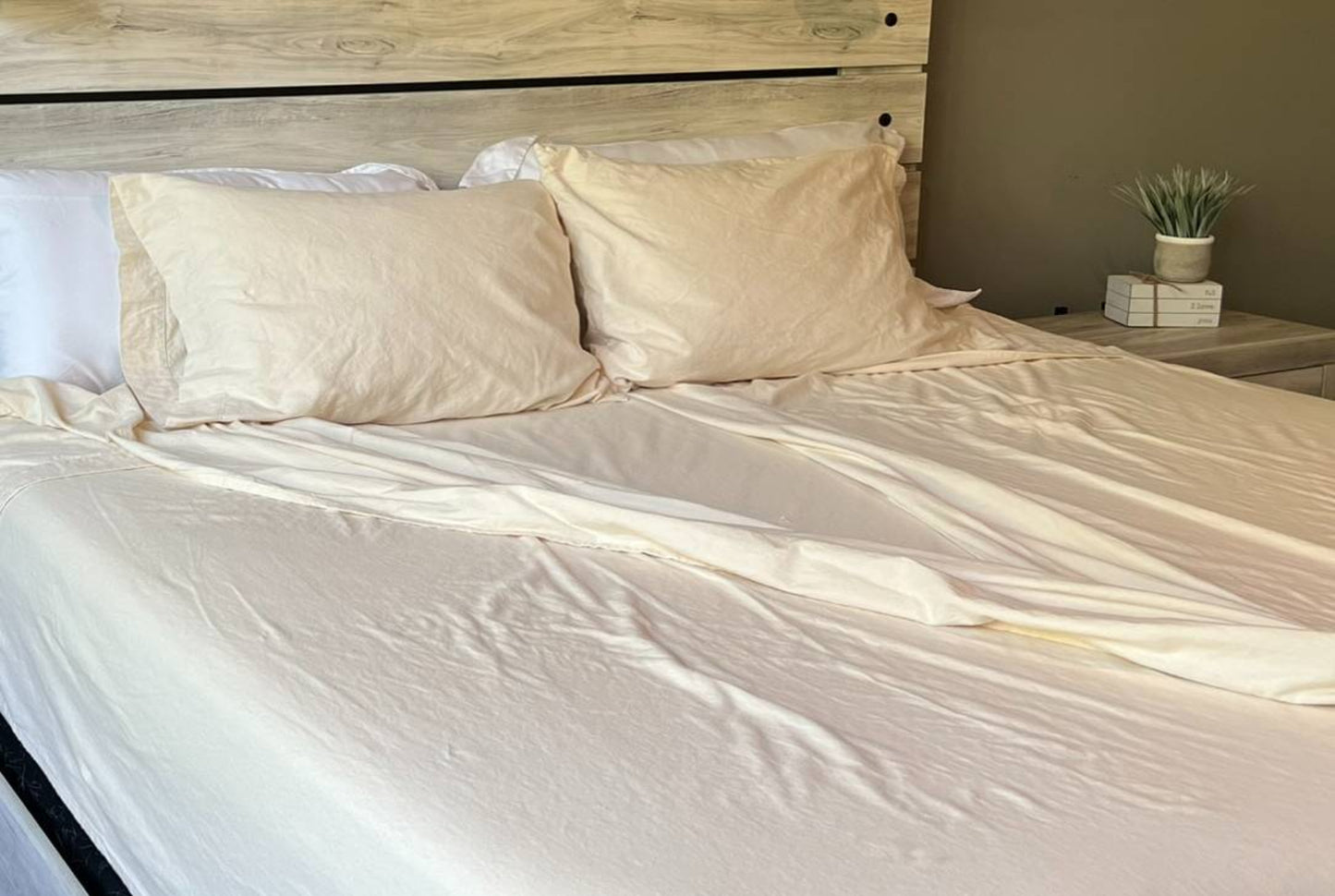 Neatly made bed with beige pillows and split sheets in a bedroom setting.