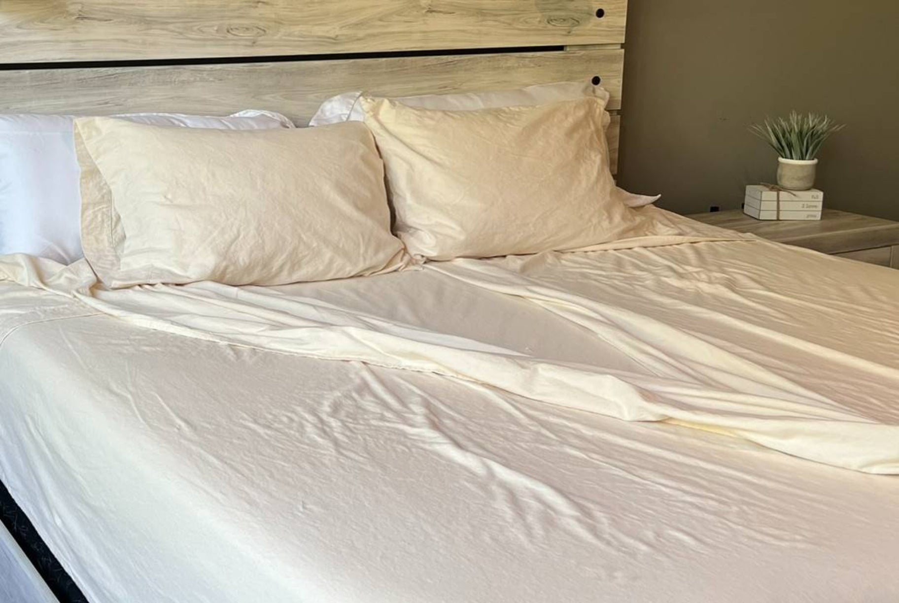 Neatly made bed with beige pillows and split sheets in a bedroom setting.