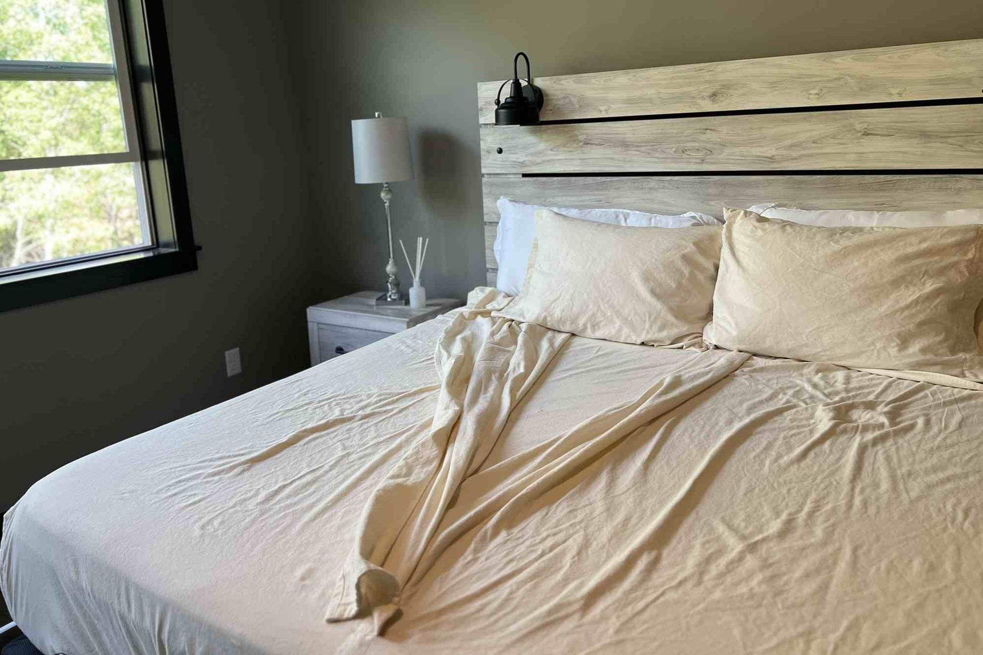 Bedroom with a bed featuring flannel split bedding and pillows, a nightstand with a lamp, and a window in the background.