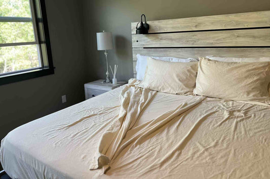 Bedroom with a bed featuring flannel split bedding and pillows, a nightstand with a lamp, and a window in the background.