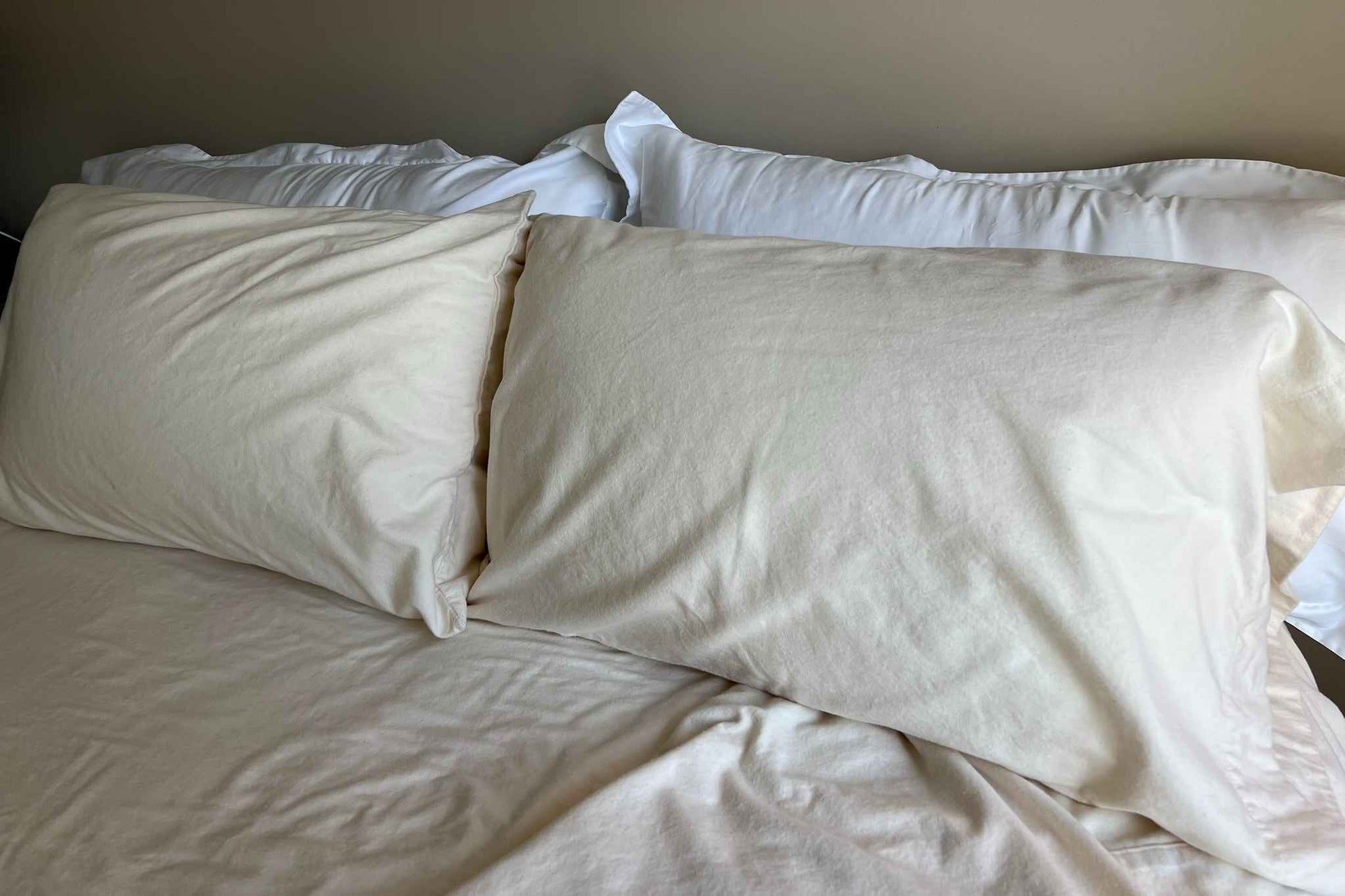 Two pillows with flannel pillowcases and two pillows with pillow shams on a bed with a neutral background