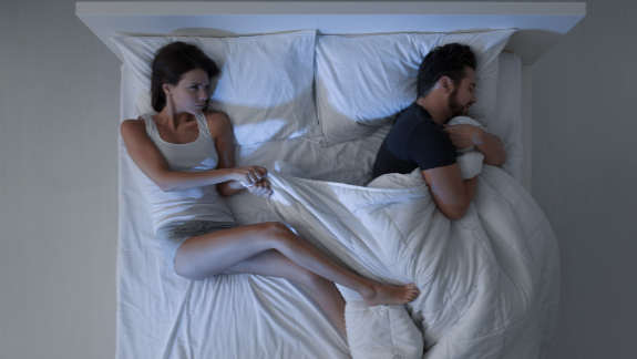 Couple in bed fighting over covers